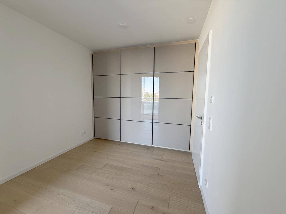 Helles Schlafzimmer mit Holzboden und einem großen, modernen Einbauschrank mit glänzenden Fronten.