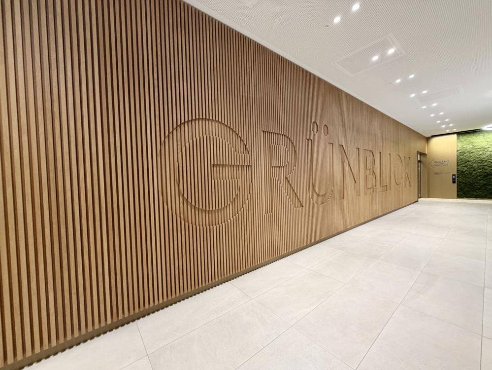Dekorative Holzwand mit dem Schriftzug "GRÜNBLICK" in einem modernen Eingangsbereich des Gebäudes.
