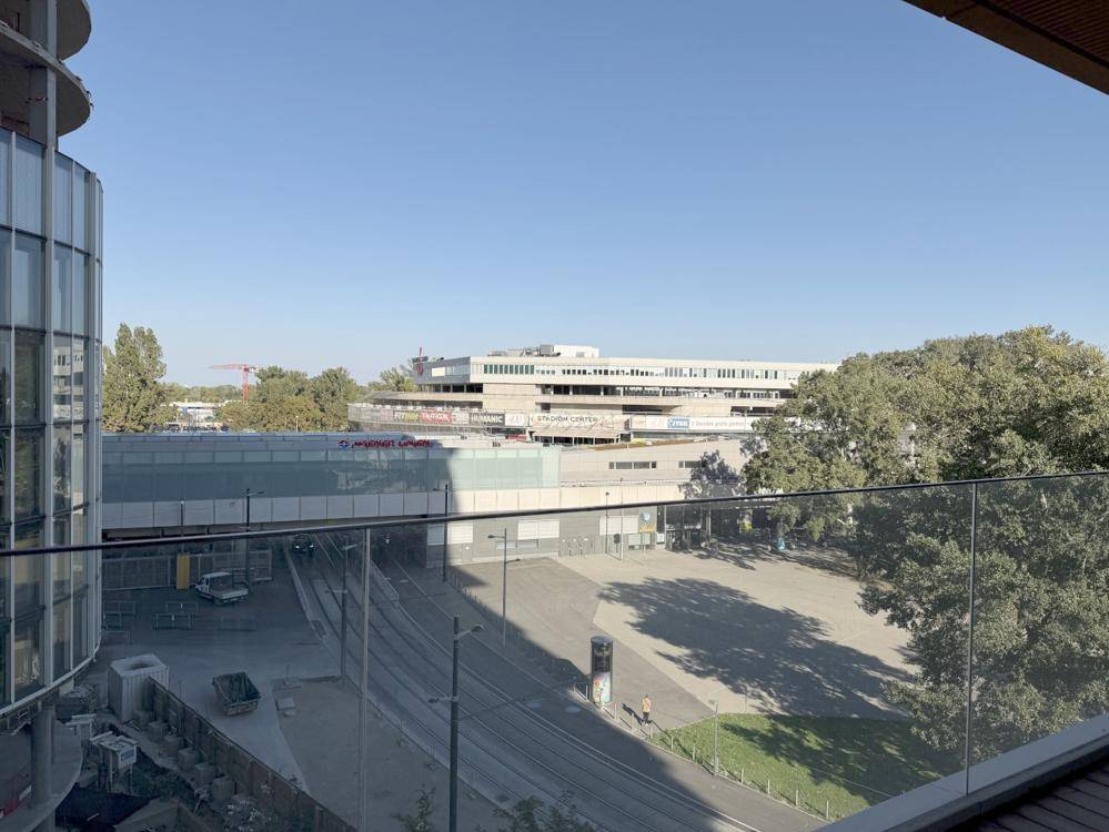 Panoramablick vom Balkon über einen urbanen Platz mit viel Grün und moderner Architektur.