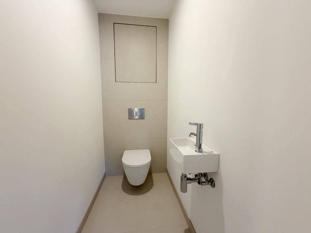 Modernes Gäste-WC mit wandhängender Toilette und kleinem Waschbecken in schlichtem Design.