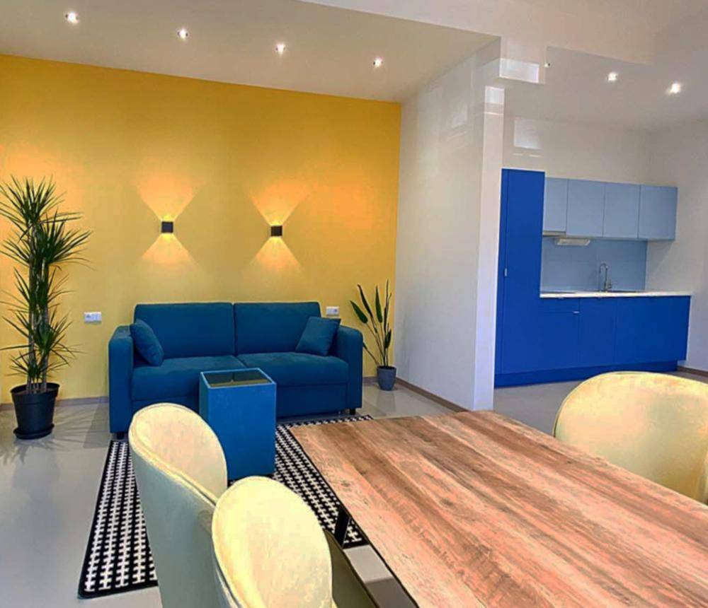 Offener Wohn- und Essbereich mit einem blauen Sofa, Holztisch und integrierter Küchenzeile.