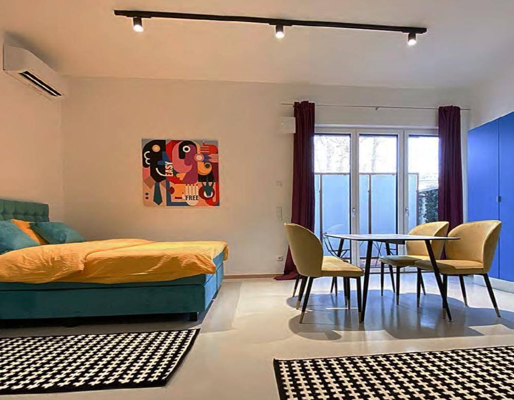 Schlafzimmer mit einem Bett, kleinem Esstisch, Klimaanlage und farbenfrohem Kunstwerk an der Wand.