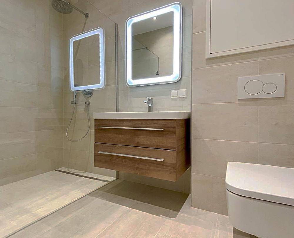 Modernes Badezimmer mit begehbarer Dusche, schwebendem Waschtisch und beleuchteten Spiegeln.