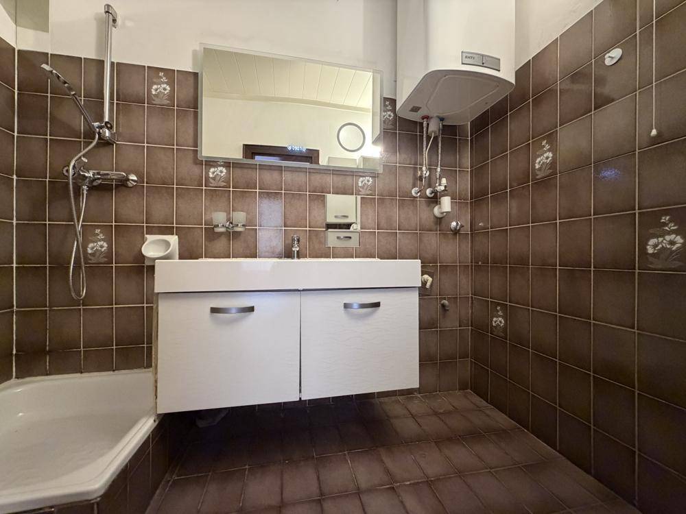Badezimmer mit braunen Fliesen, Badewanne und modernem Waschtisch, funktional und gut beleuchtet.