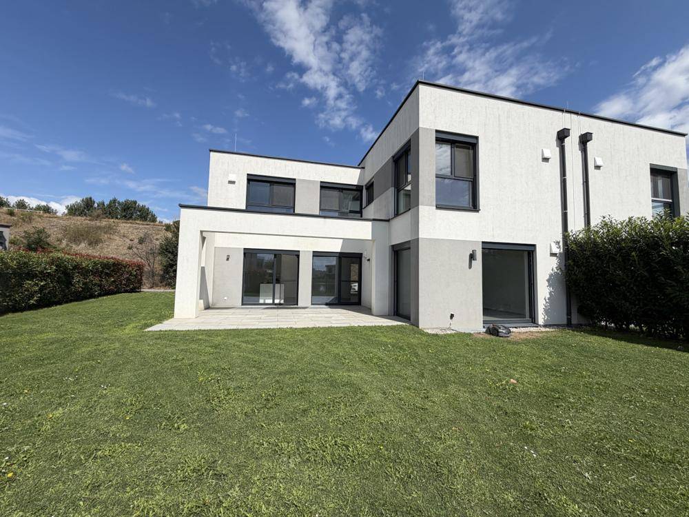 Moderne Hausfassade mit großen Fensterflächen und weitläufigem Gartenbereich.