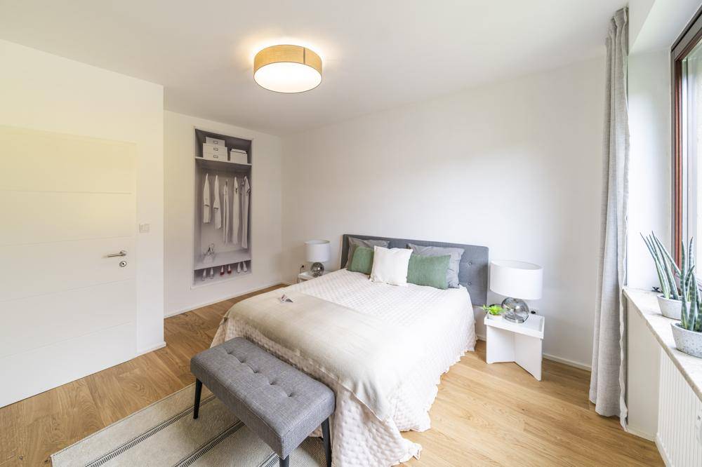 Helles Schlafzimmer mit Doppelbett, Holzboden und integriertem Kleiderschrank.