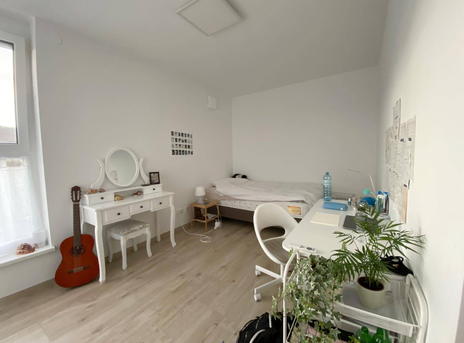 Gemütliches Schlafzimmer mit Bett, Schminktisch, Schreibtisch und einer Gitarre, hell und freundlich.