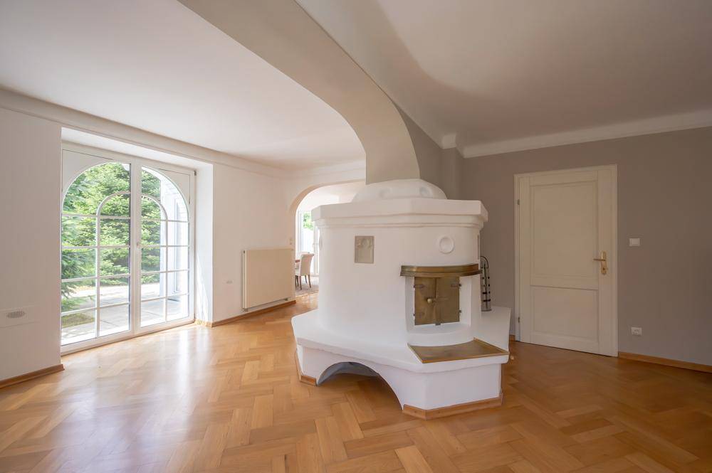 Geräumiges Wohnzimmer mit traditionellem Kachelofen und Zugang zum Garten.