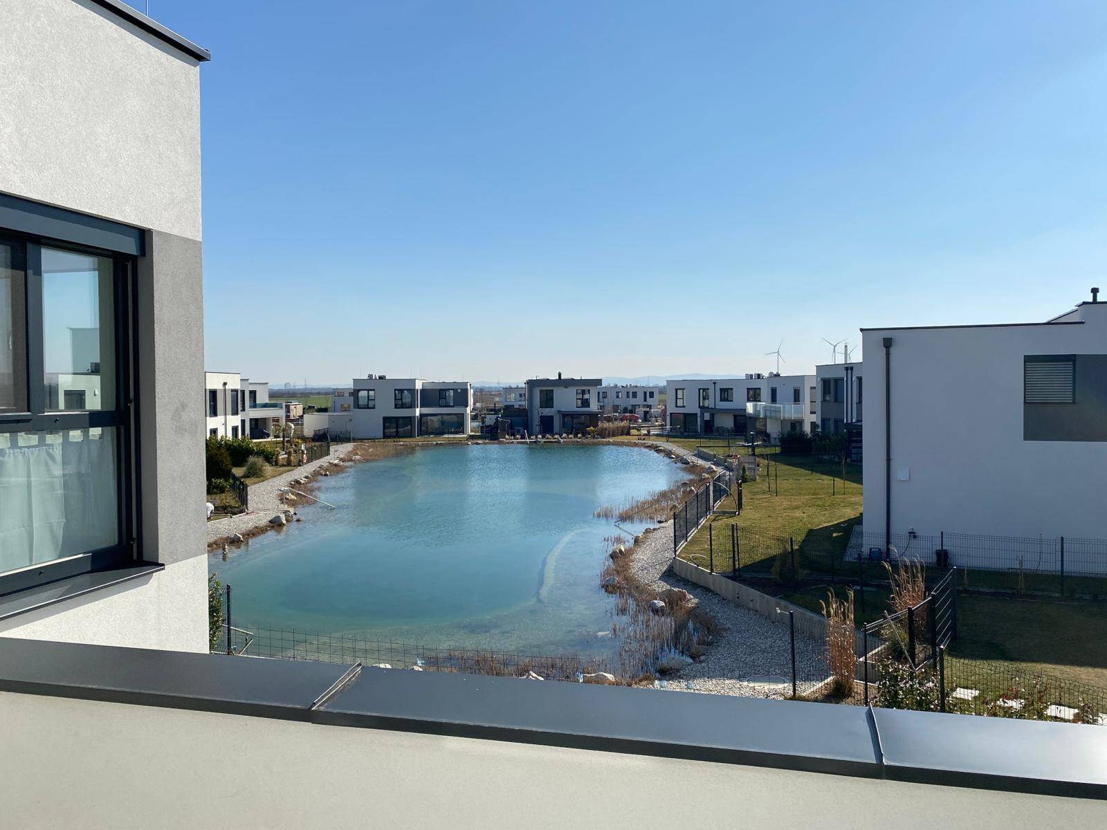 Panoramablick von einem Balkon auf einen künstlichen See, umgeben von modernen Wohngebäuden.