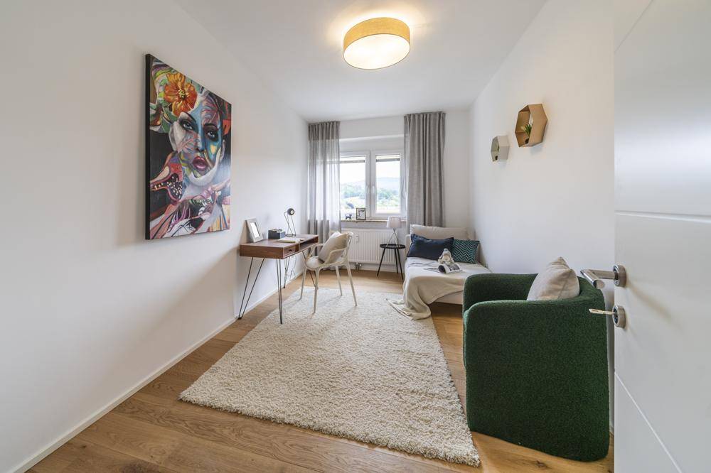 Helles Arbeitszimmer mit Holzboden, Schreibtisch und farbenfrohem Kunstwerk an der Wand.