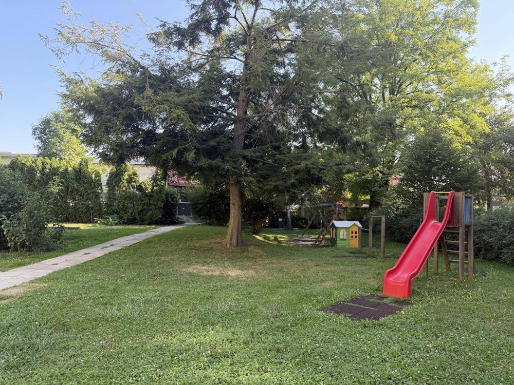 Grüner Gartenbereich mit Rutsche und Spielhaus, ideal für Kinder zum Spielen im Freien.