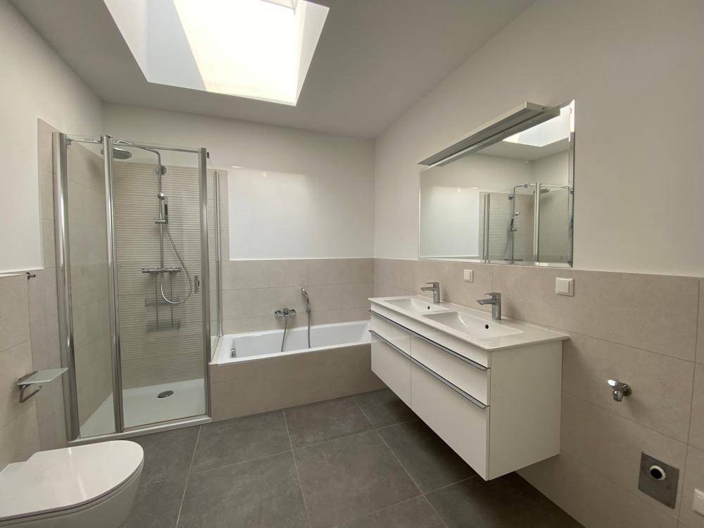 Helles Badezimmer mit Doppelwaschbecken, Badewanne, Dusche und Dachfenster für viel Tageslicht.