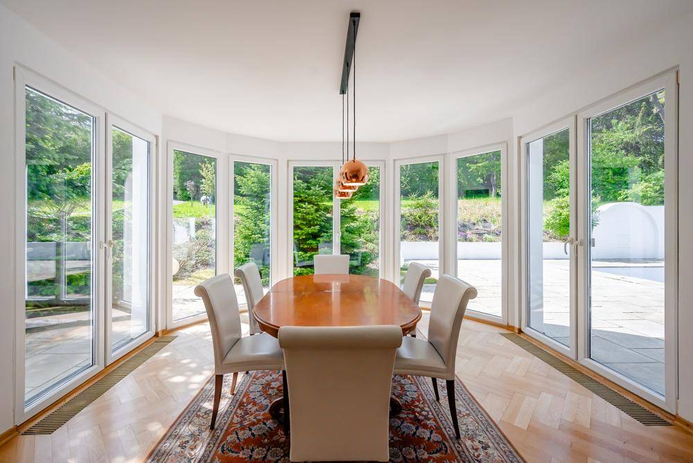 Lichtdurchfluteter Essbereich mit elegantem Holztisch und Stühlen, umgeben von Fenstern.
