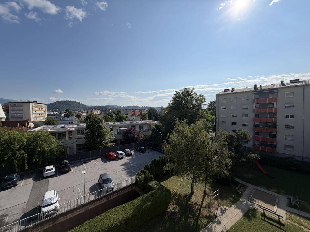 Blick auf die Umgebung mit Parkplatz, Bäumen und Wohngebäuden unter blauem Himmel.