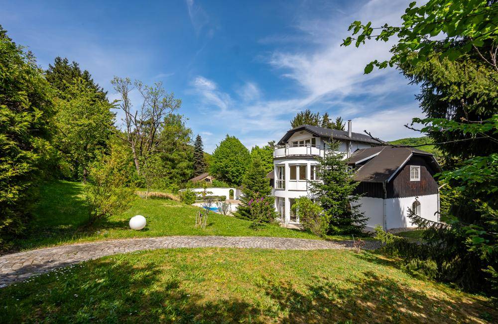 Malerischer Gartenweg führt zur Villa, umgeben von üppigem Grün und Bäumen.
