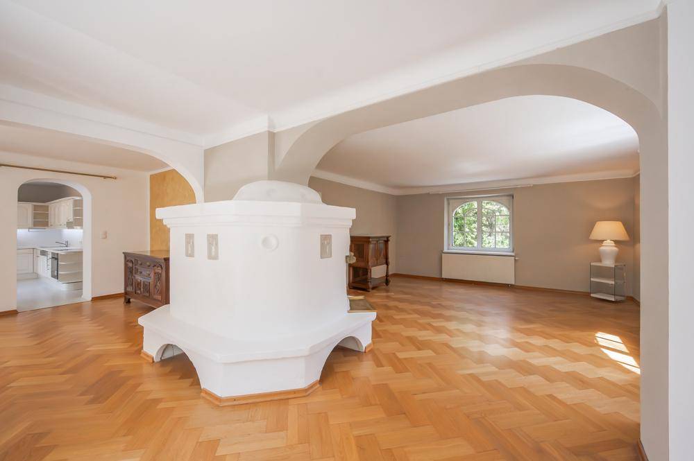 Großzügiges Wohnzimmer mit Parkettboden, Kachelofen und Blick ins Grüne.
