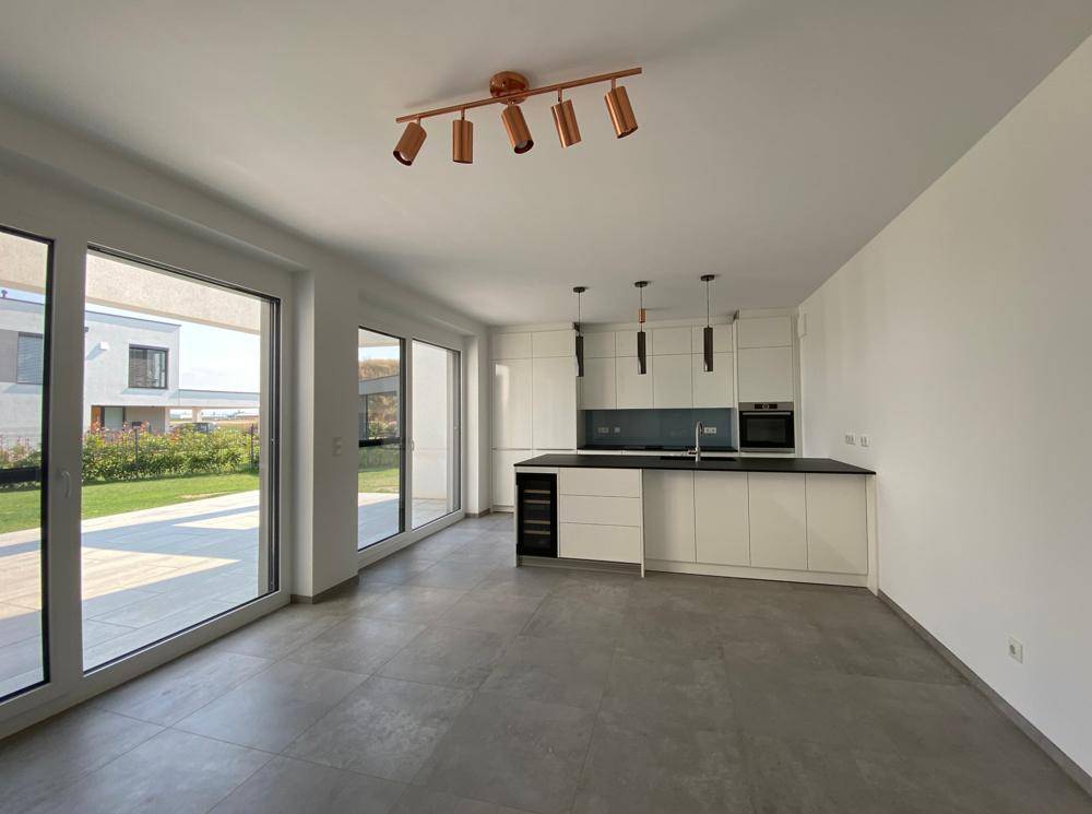 Geräumiger offener Wohnbereich mit integrierter Küche, Fliesenboden und großen Fensterfronten.