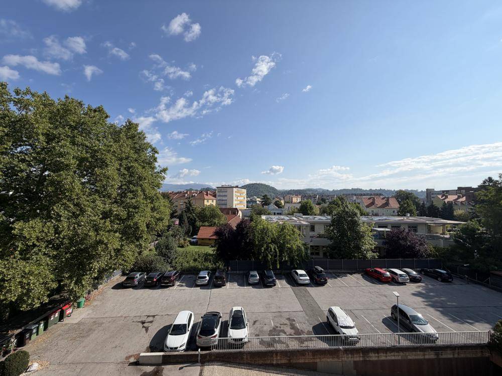 Weitläufiger Blick über einen Parkplatz und die Stadtlandschaft mit Bergen im Hintergrund.