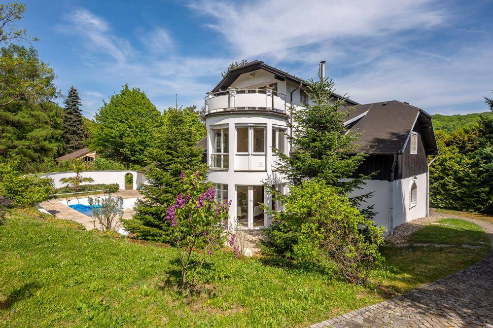 Elegante Villa mit einem kleinen Poolbereich, umgeben von blühenden Sträuchern und Bäumen.