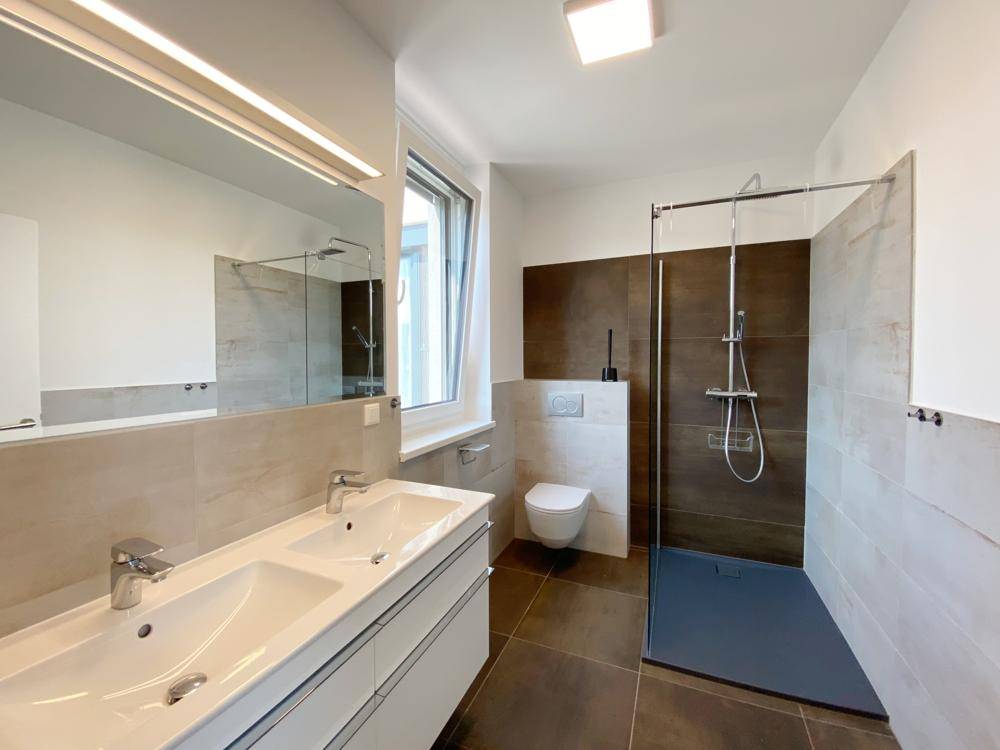Modernes Badezimmer mit Doppelwaschbecken, großer Dusche und Fenster für natürliche Belüftung.