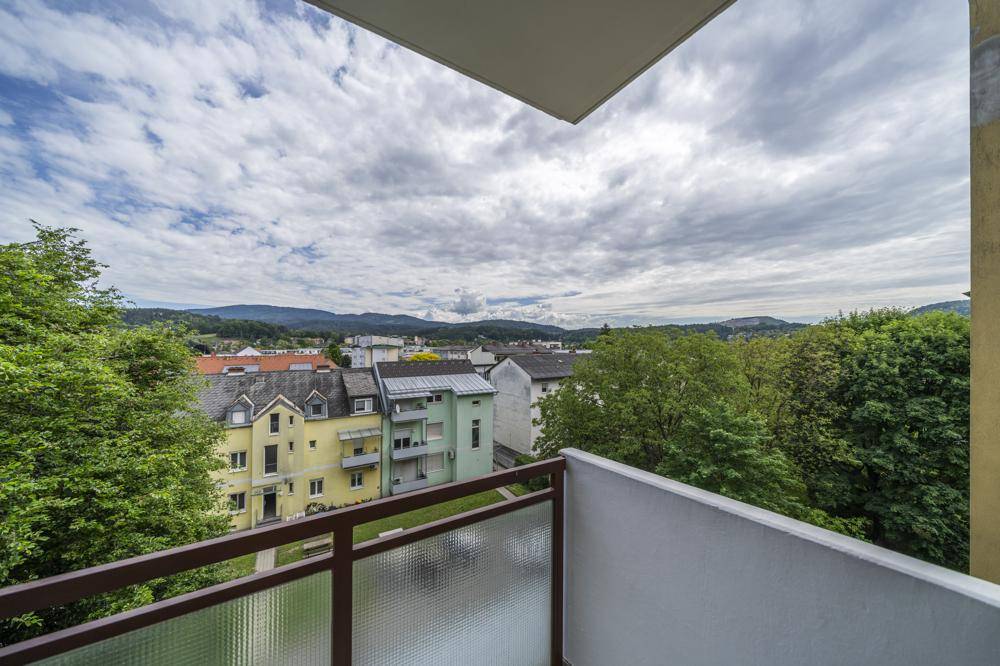 Weitläufiger Blick vom Balkon über die Dächer der Stadt und grüne Hügel.