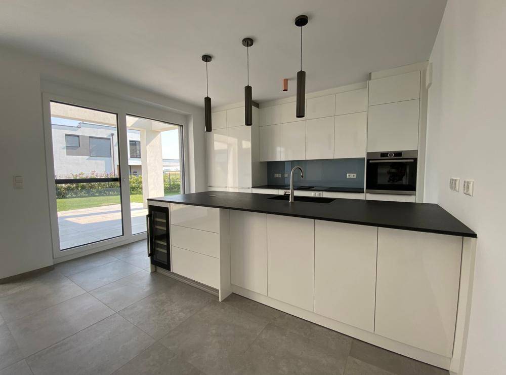 Moderne Einbauküche mit weiß-glänzenden Fronten, dunkler Arbeitsplatte und Zugang zum Garten.