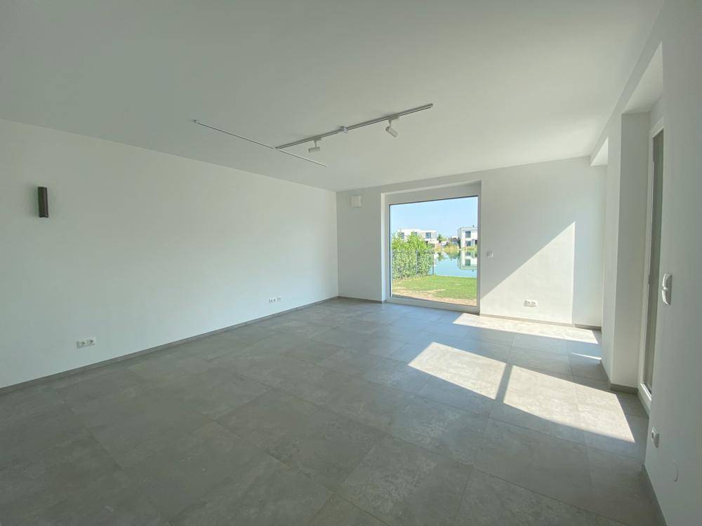 Heller Wohnraum mit Fliesenboden und großen Fensterfronten, die viel Tageslicht hereinlassen.