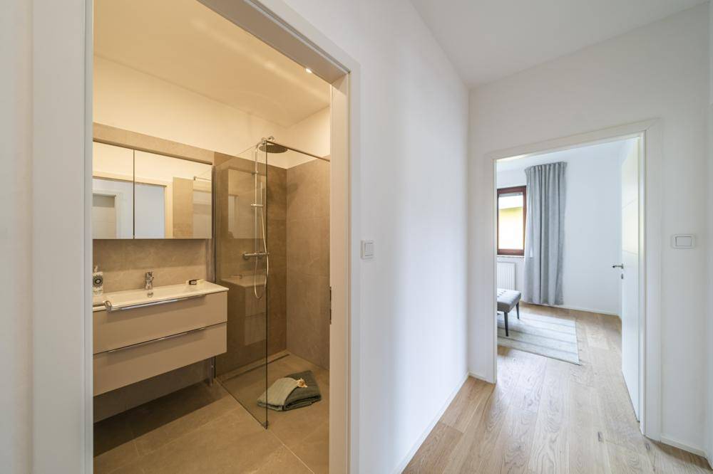 Heller Flur mit Holzboden, der zu einem modernen Badezimmer und Schlafzimmer führt.