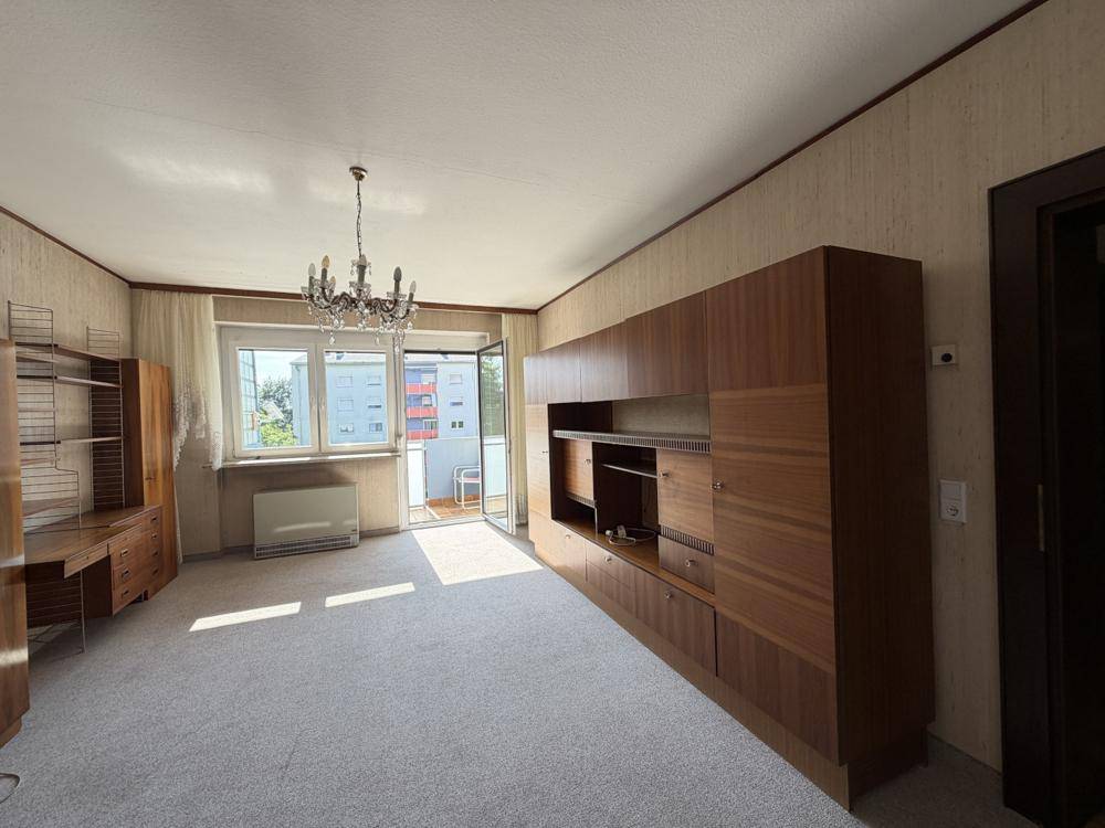 Geräumiges Wohnzimmer mit Teppichboden, Holzmöbeln und Zugang zu einem Balkon, hell und einladend.