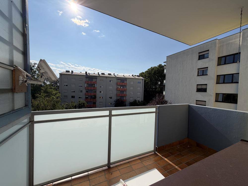 Balkon mit Milchglasgeländer und Blick auf umliegende Wohngebäude unter strahlendem Sonnenschein.