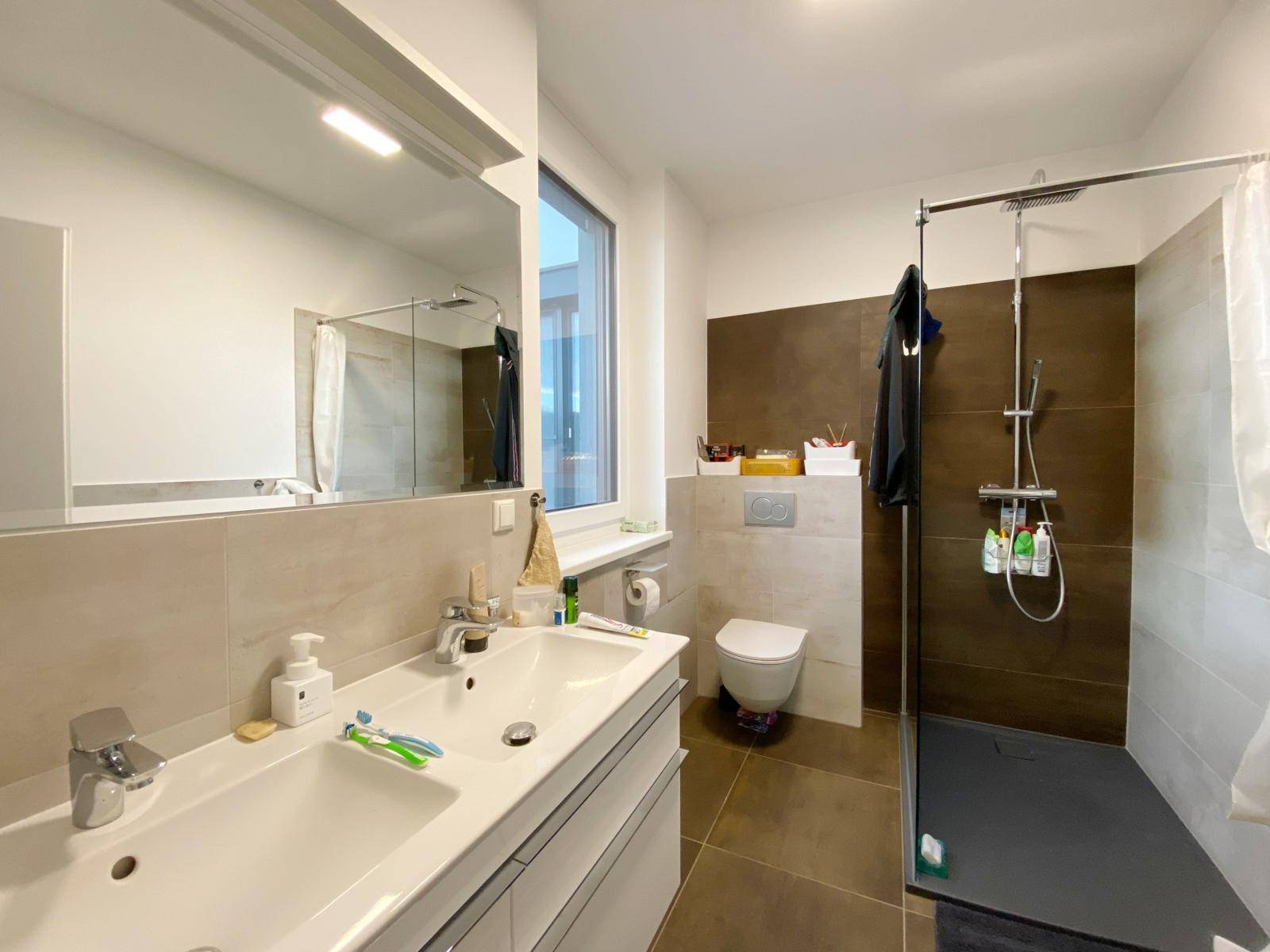 Modernes Badezimmer mit großer Dusche, Toilette, Doppelwaschbecken und Fenster für Tageslicht.