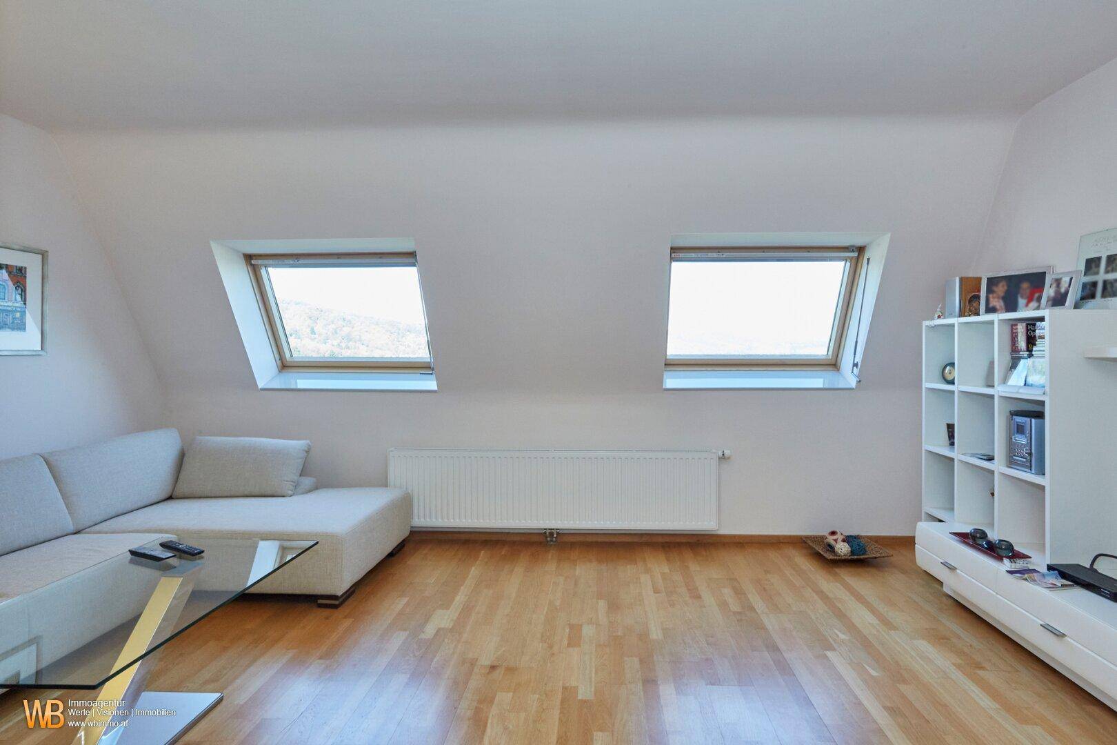 Helles Wohnzimmer im Dachgeschoss mit zwei Dachfenstern, Holzboden und modernem Sofa.