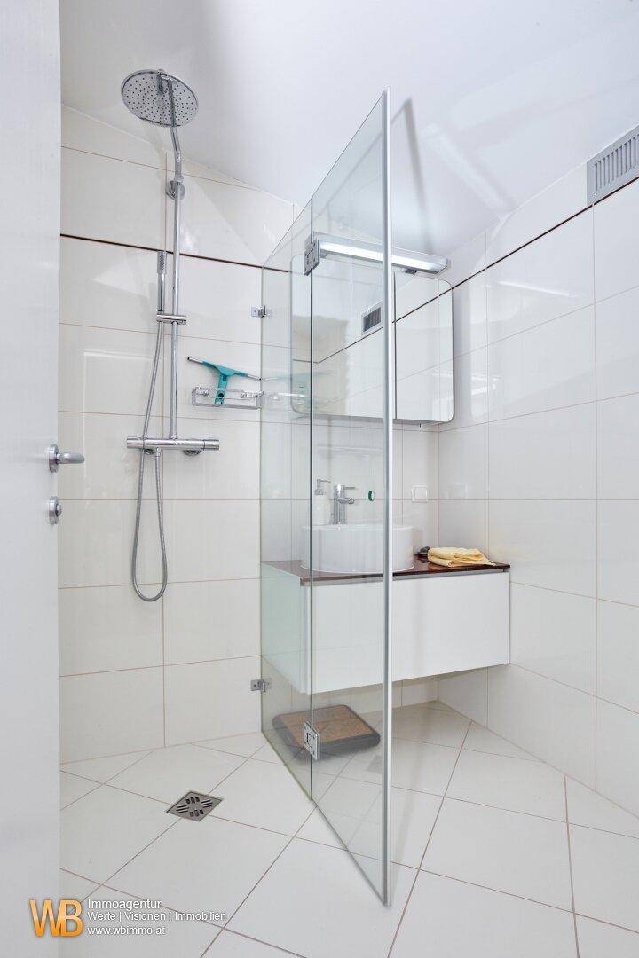Modernes Badezimmer mit weiß gefliesten Wänden, begehbarer Dusche und elegantem Waschbecken.