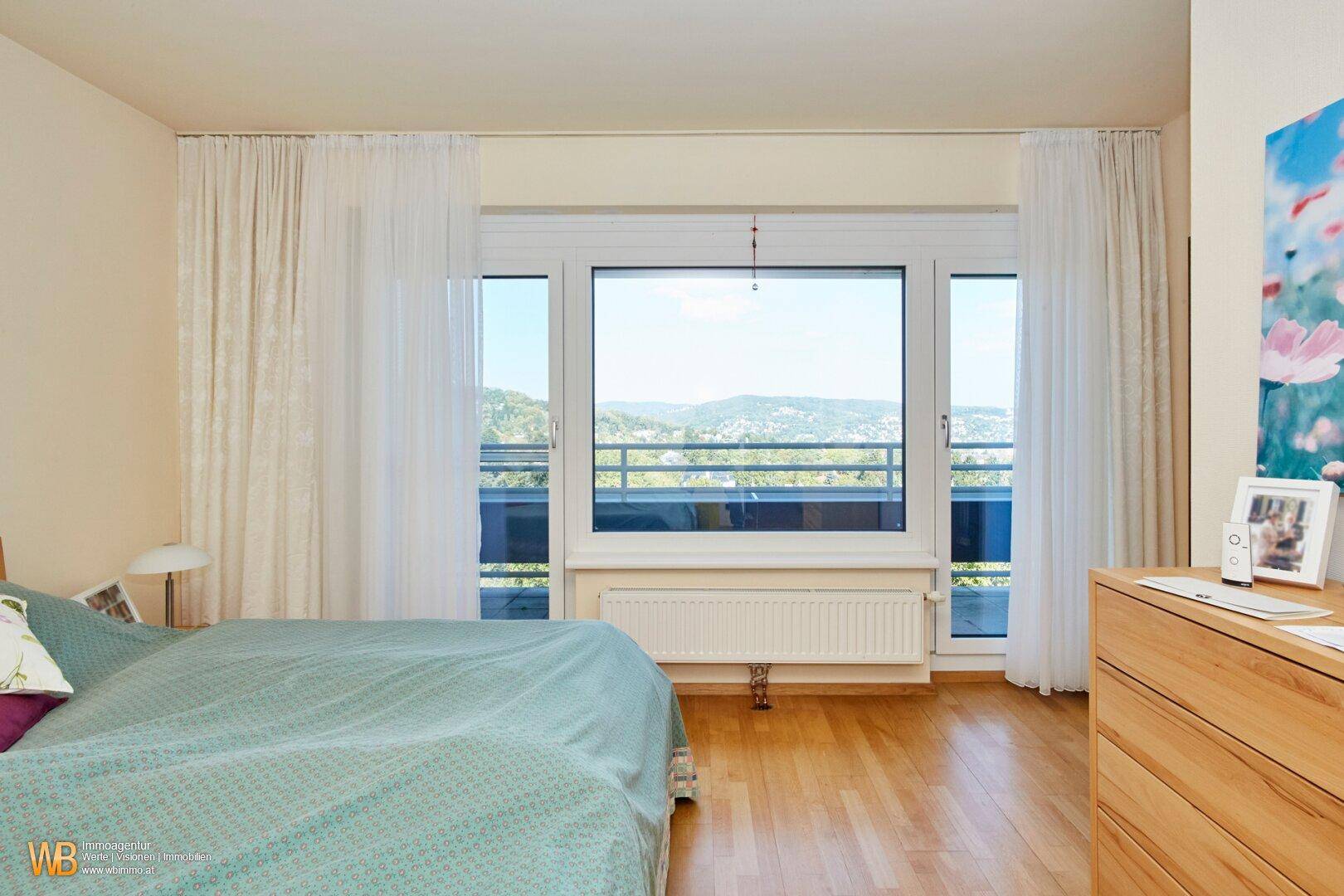 Helles Schlafzimmer mit Holzboden, großem Fenster und Zugang zu einem Außenbereich.