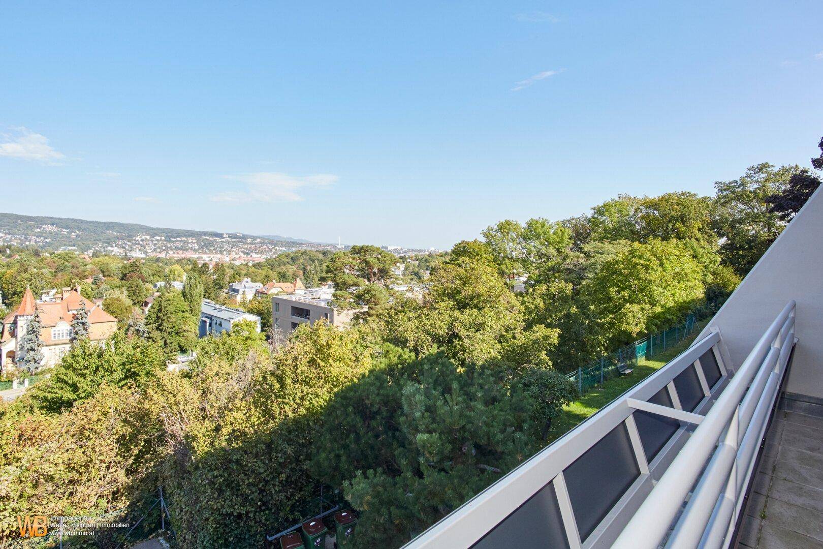 Blick vom Balkon über eine grüne Wohngegend mit Bäumen und einem weiten Horizont.