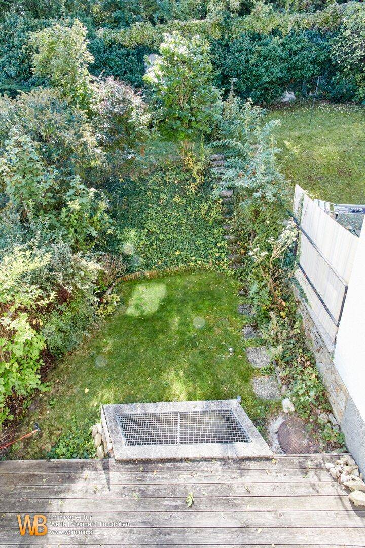 Kleiner, gepflegter Gartenbereich mit Rasenfläche und Holzdeck, umgeben von üppigem Grün.