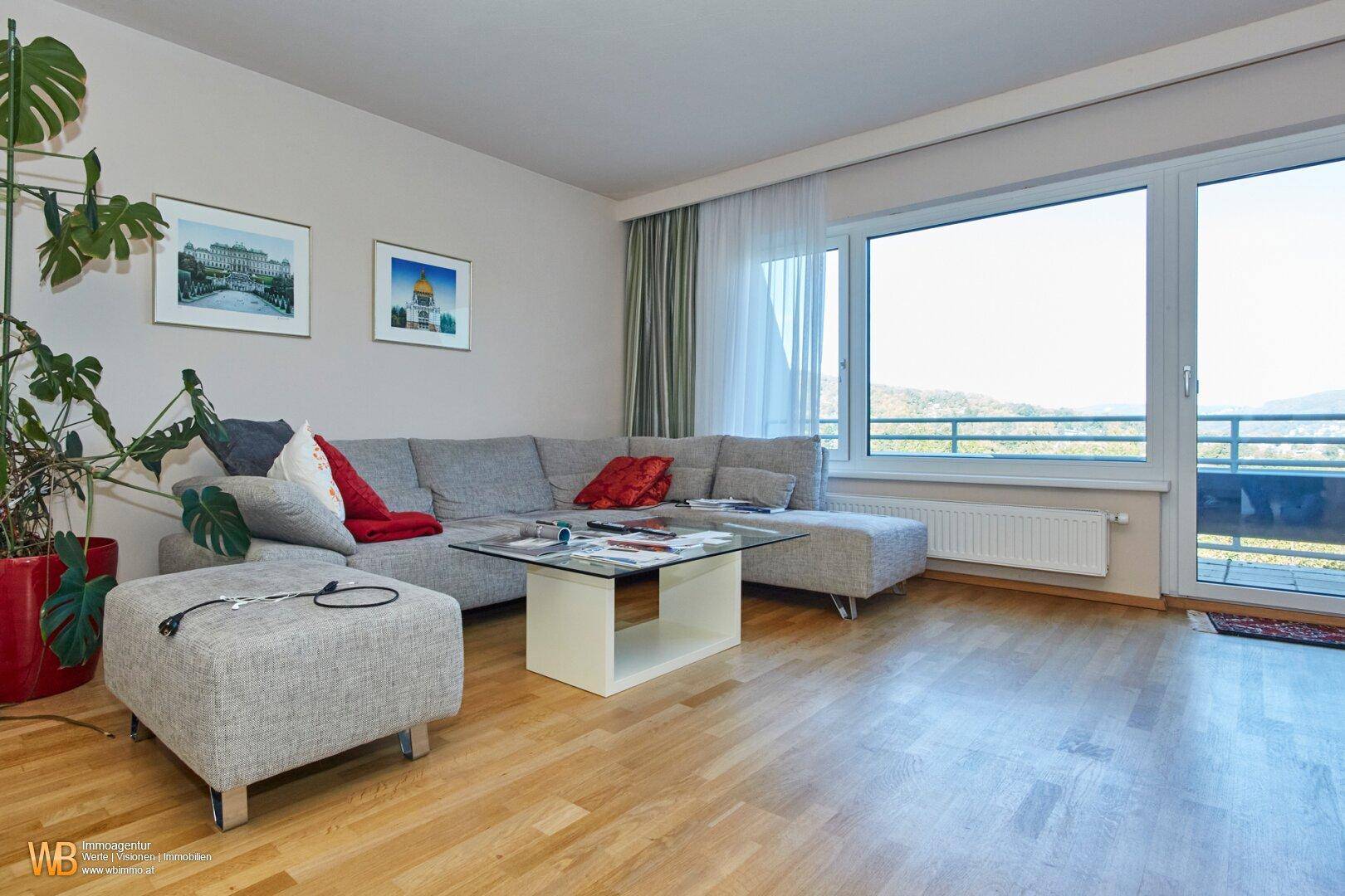 Helles Wohnzimmer mit beigem Sofa, Holzboden und großem Fenster mit Zugang zum Balkon.