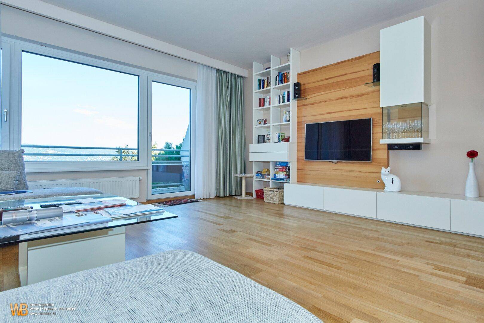 Modernes Wohnzimmer mit Holzboden, großem Fenster und einer eleganten TV-Wandgestaltung.