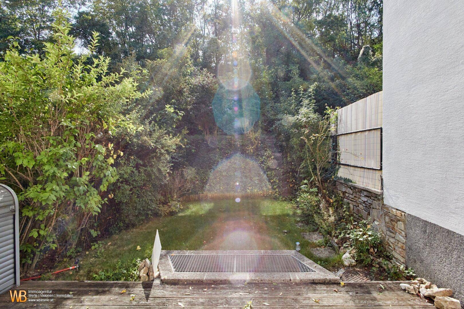 Sonnige Gartenfläche mit üppigem Grün und einer Holzterrasse, ideal zum Entspannen.