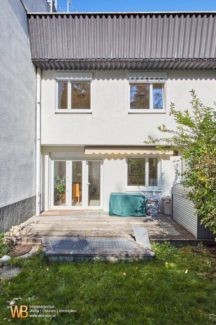 Rückseite des Hauses mit einer Holzterrasse und direktem Zugang zum grünen Garten.