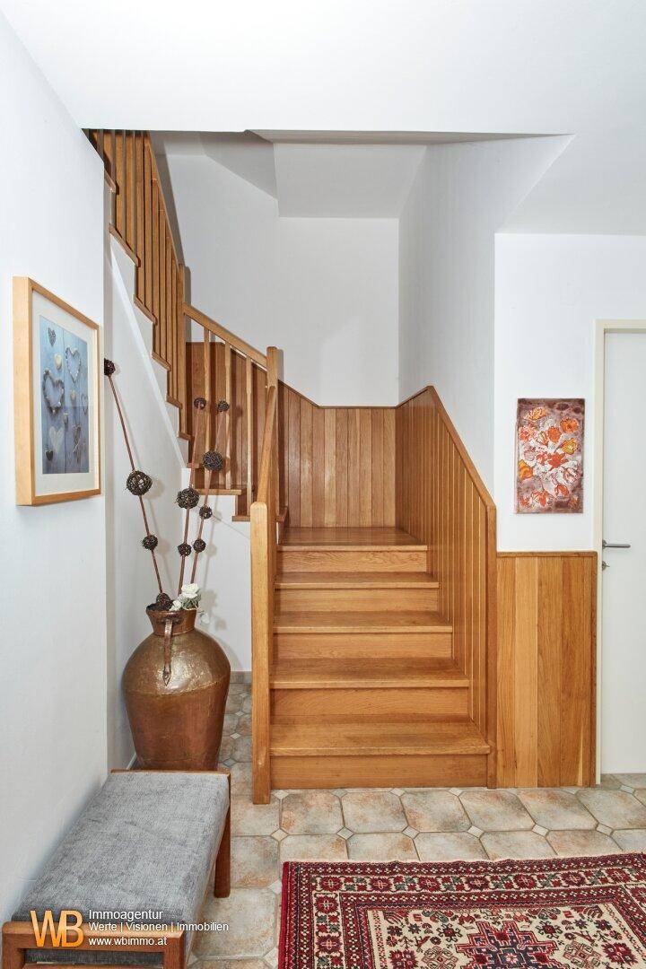 Einladender Eingangsbereich mit Holztreppe, Fliesenboden und dekorativer Vase.