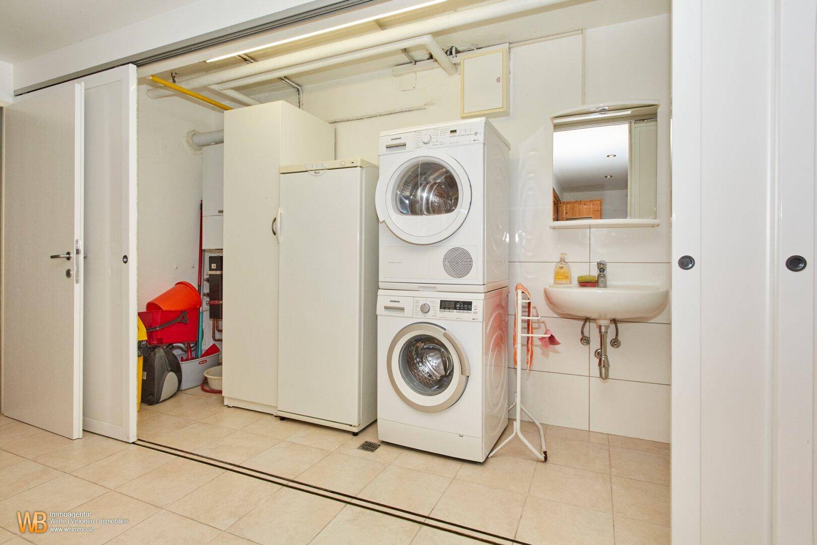 Praktischer Hauswirtschaftsraum mit Waschmaschine, Trockner, Waschbecken und viel Stauraum.