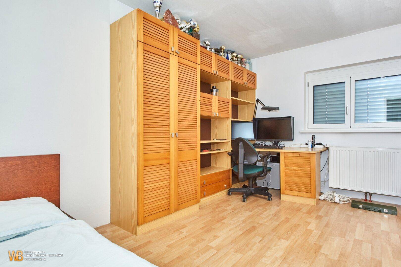 Schlafzimmer mit integrierten Holzschränken, Schreibtischbereich und hellem Holzboden.