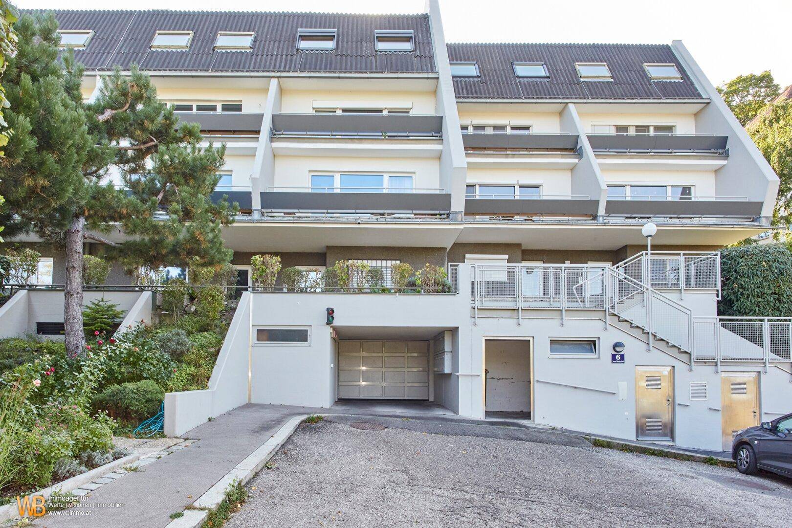 Moderne Reihenhausfassade mit Garagenzugang, Außentreppen und gepflegter Bepflanzung.