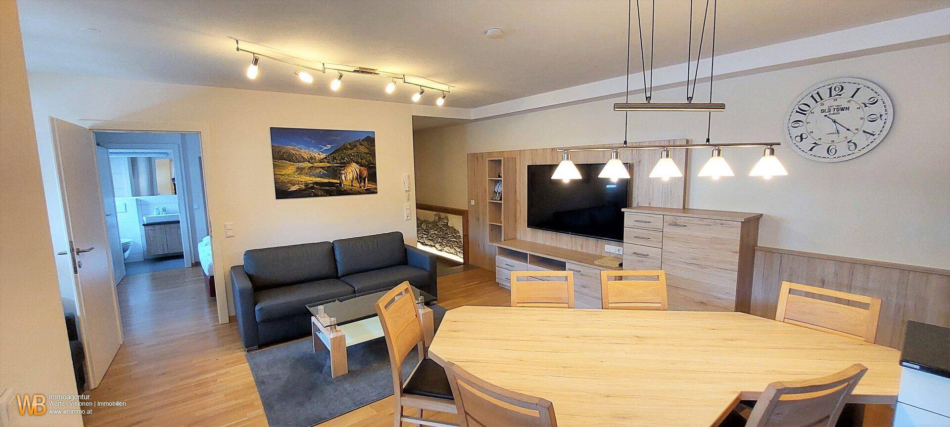 Helles Wohn- und Esszimmer mit Holzboden, moderner Einrichtung und Blick in den Flur.