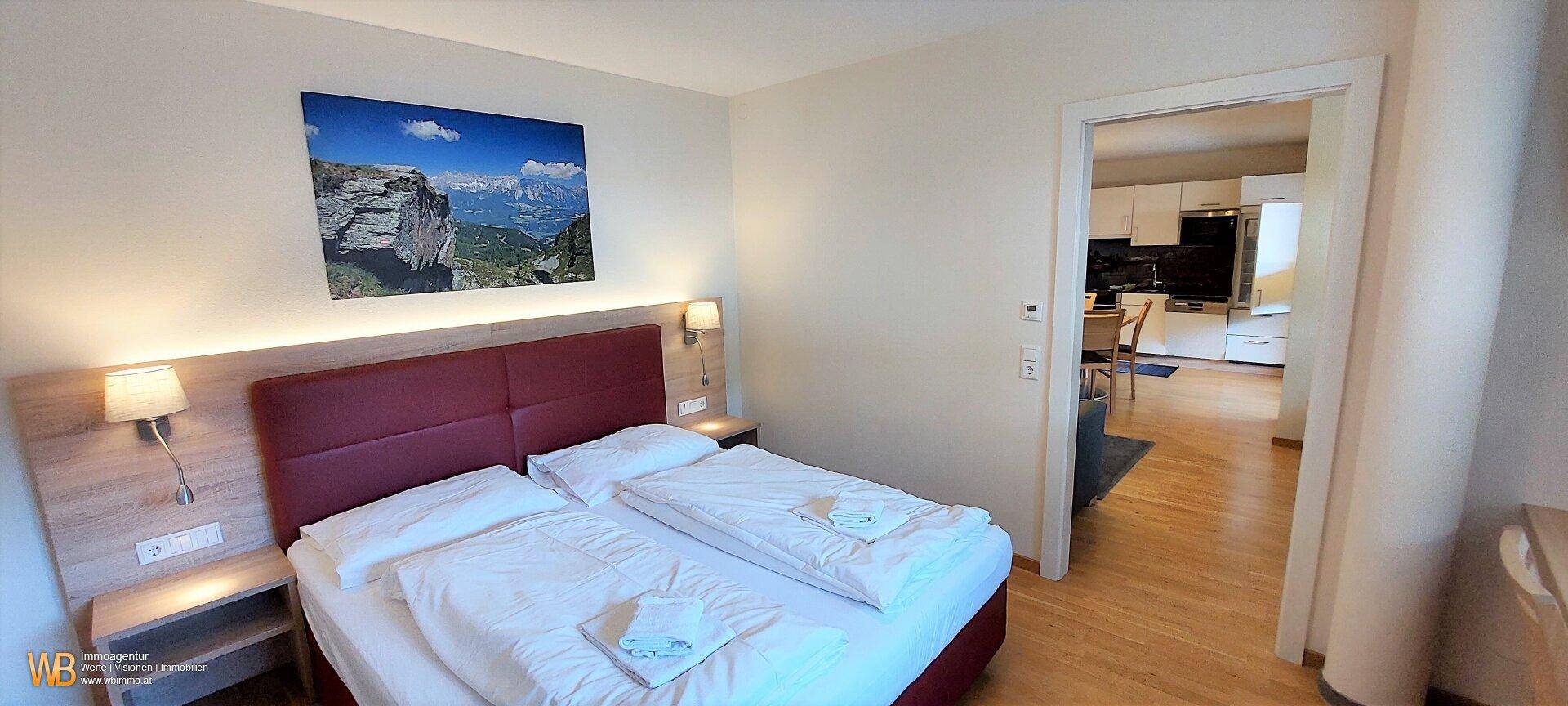 Gemütliches Schlafzimmer mit Doppelbett, Holzboden und Zugang zur Küche.