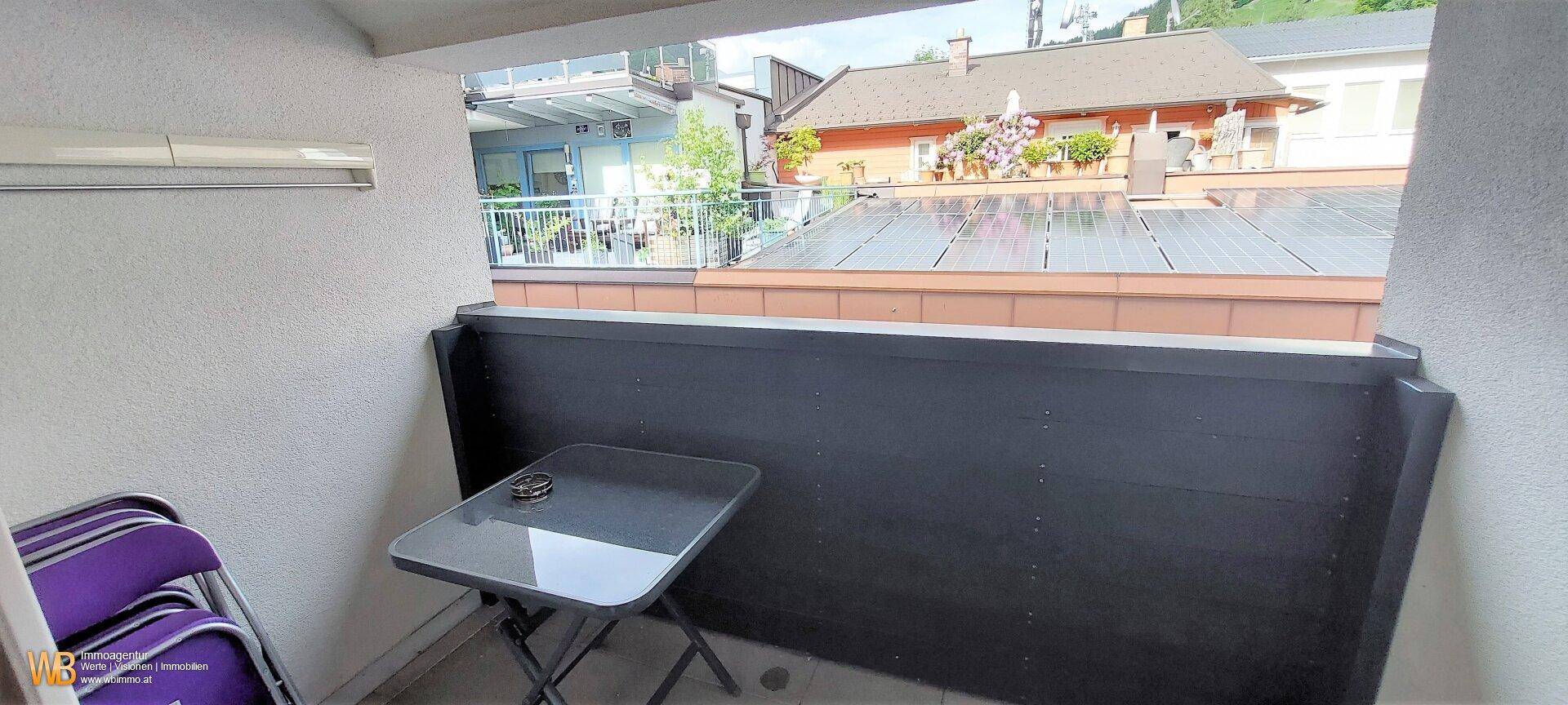 Kleiner Balkon mit Tisch und Stühlen, bietet Blick auf umliegende Gebäude und Solarpaneele.