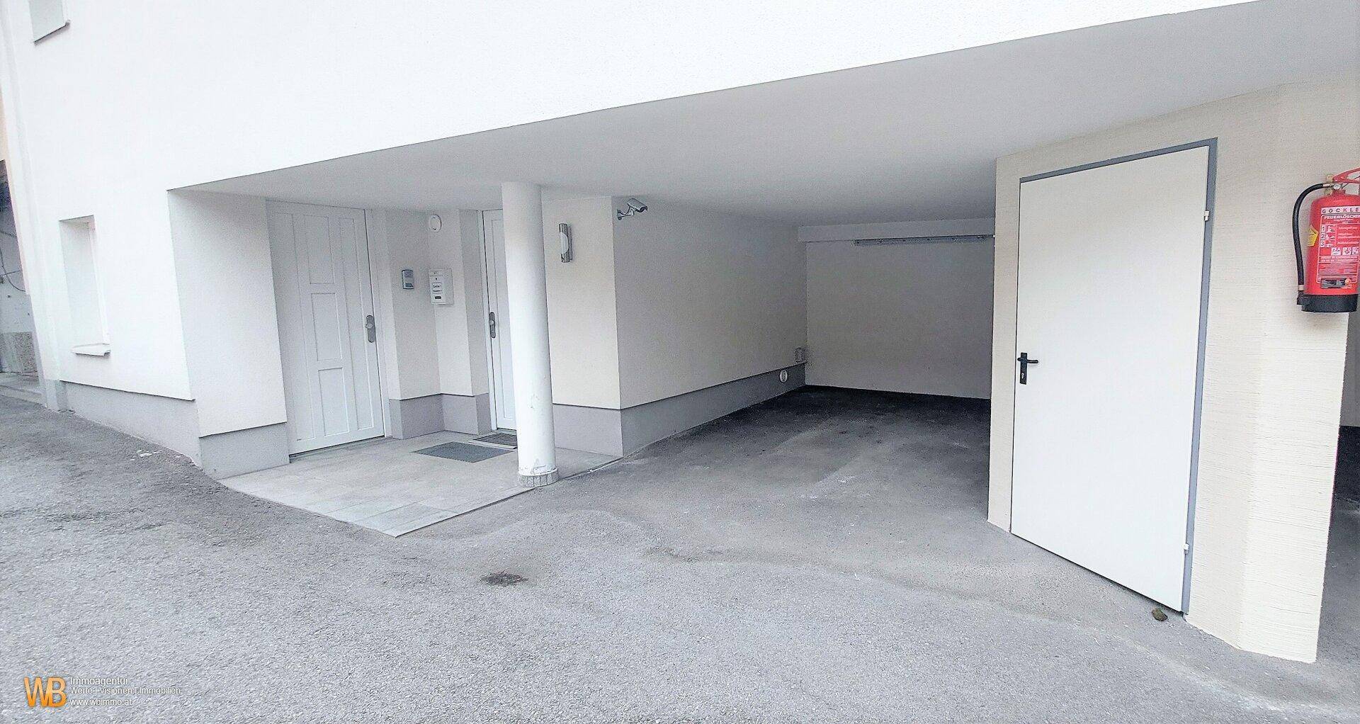 Überdachter Eingangsbereich und Garagenzufahrt mit Feuerlöscher.
