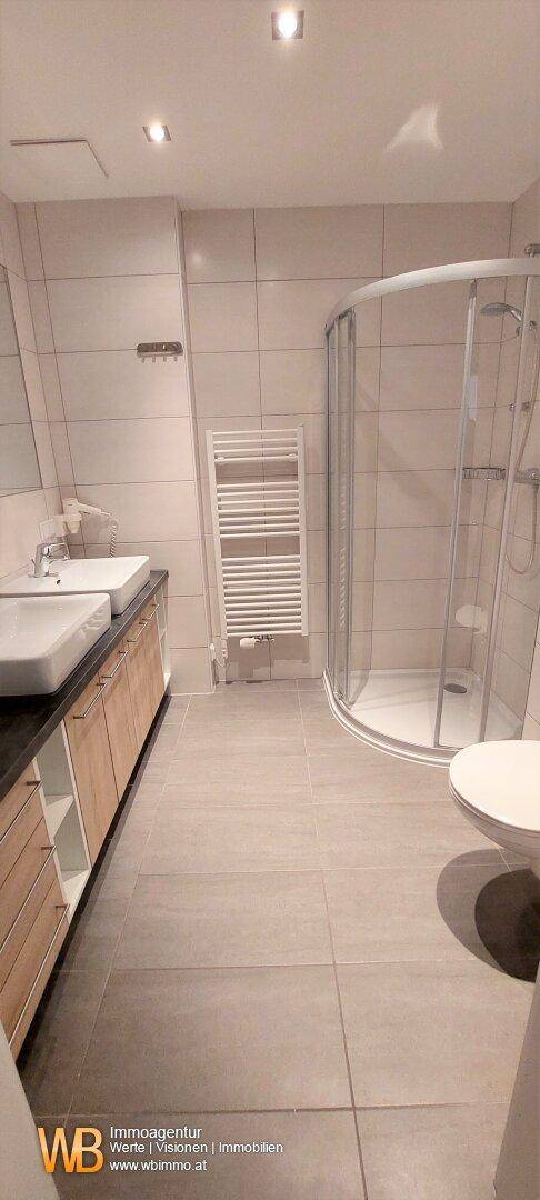 Modernes Badezimmer mit Doppelwaschbecken, Duschkabine und beheiztem Handtuchhalter.