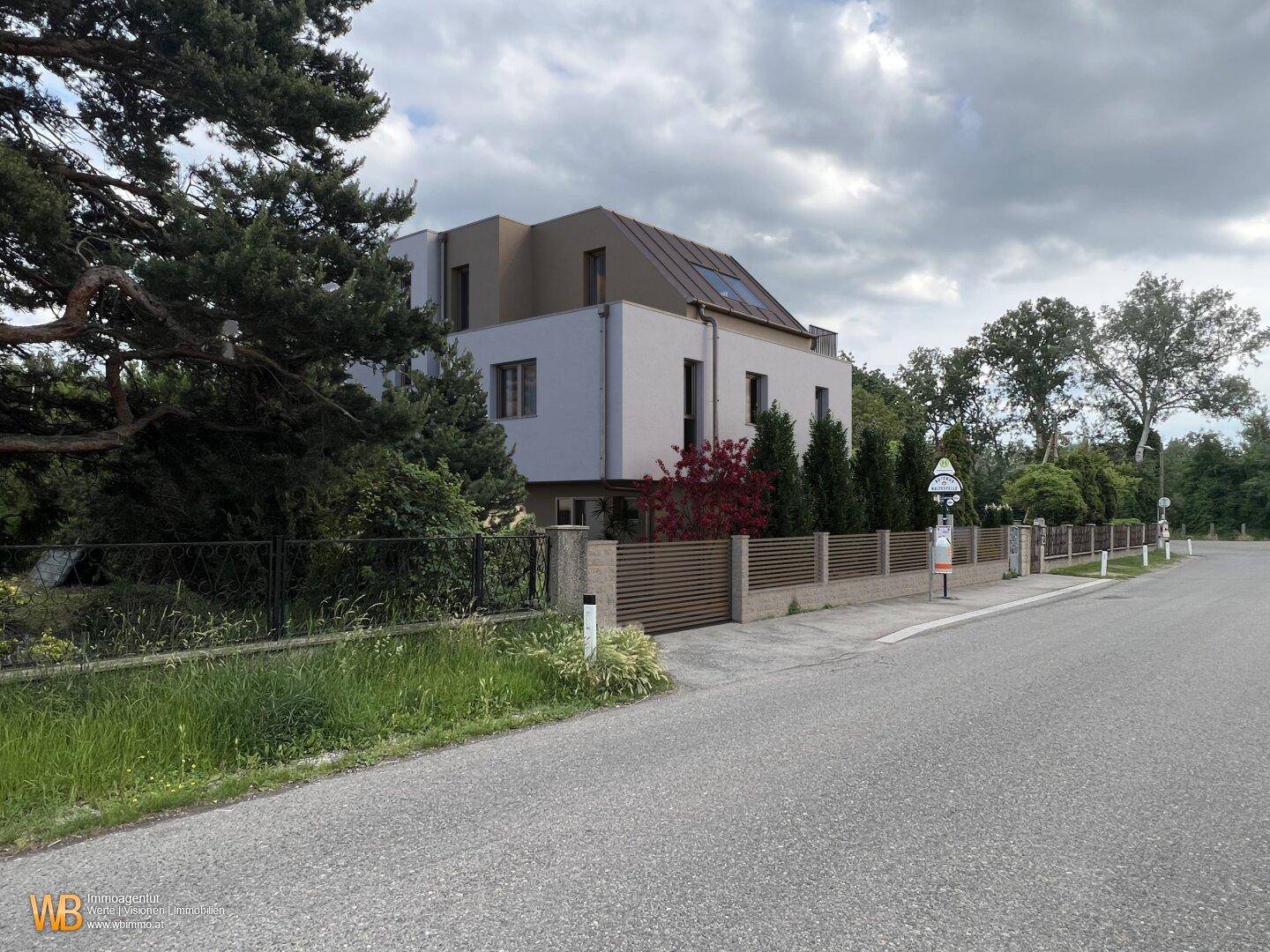 Außenansicht der modernen Wohnanlage von der Straße aus mit Bäumen und Zaun.